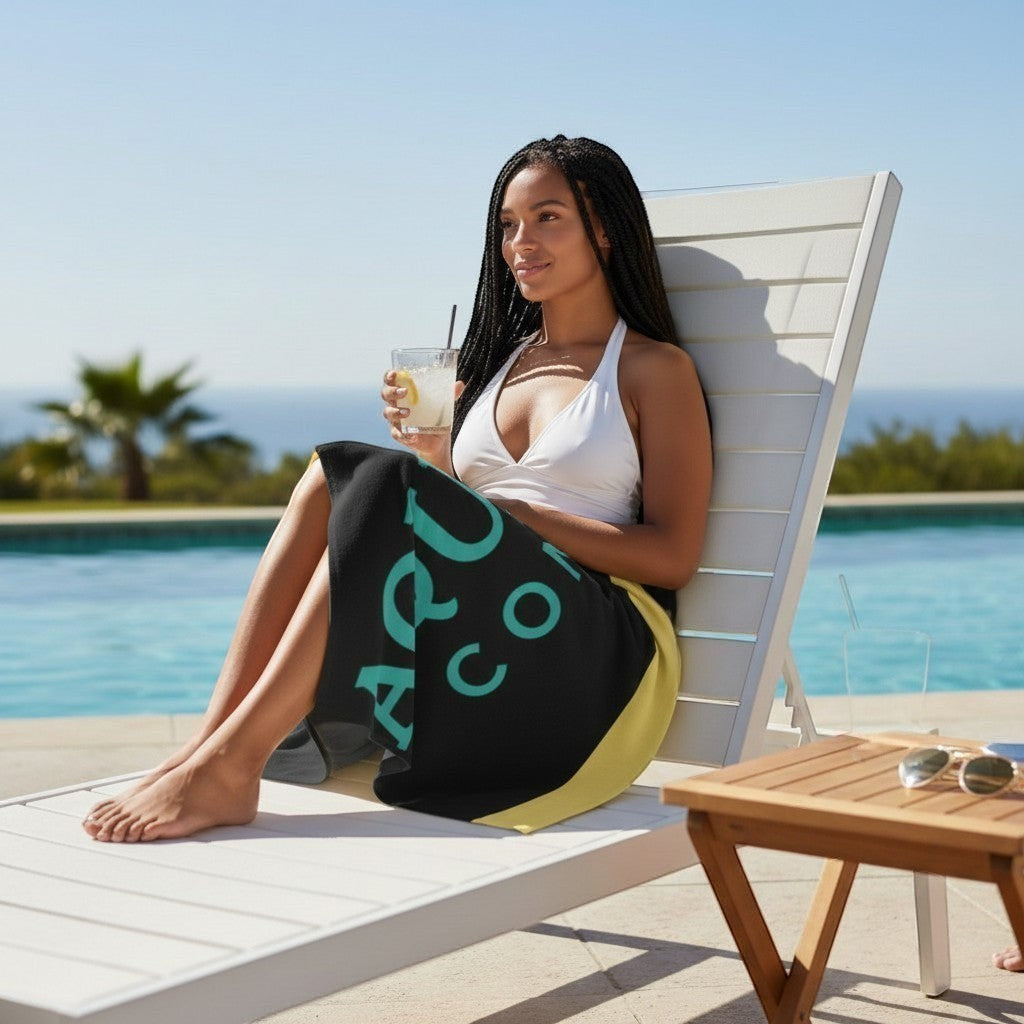 Woman relaxing on a lounge chair by a pool with an Aqua Sol Company beach towel featuring aqua and yellow accents.
